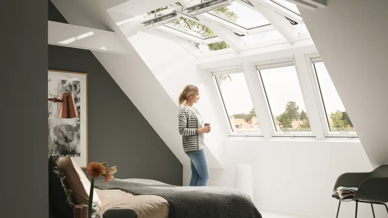 Eine Frau schaut nach draußen und steht im Sonnenlicht , das durch eine Vielzahl an Dachfenstern hereinkommt. | VELUX Magazin