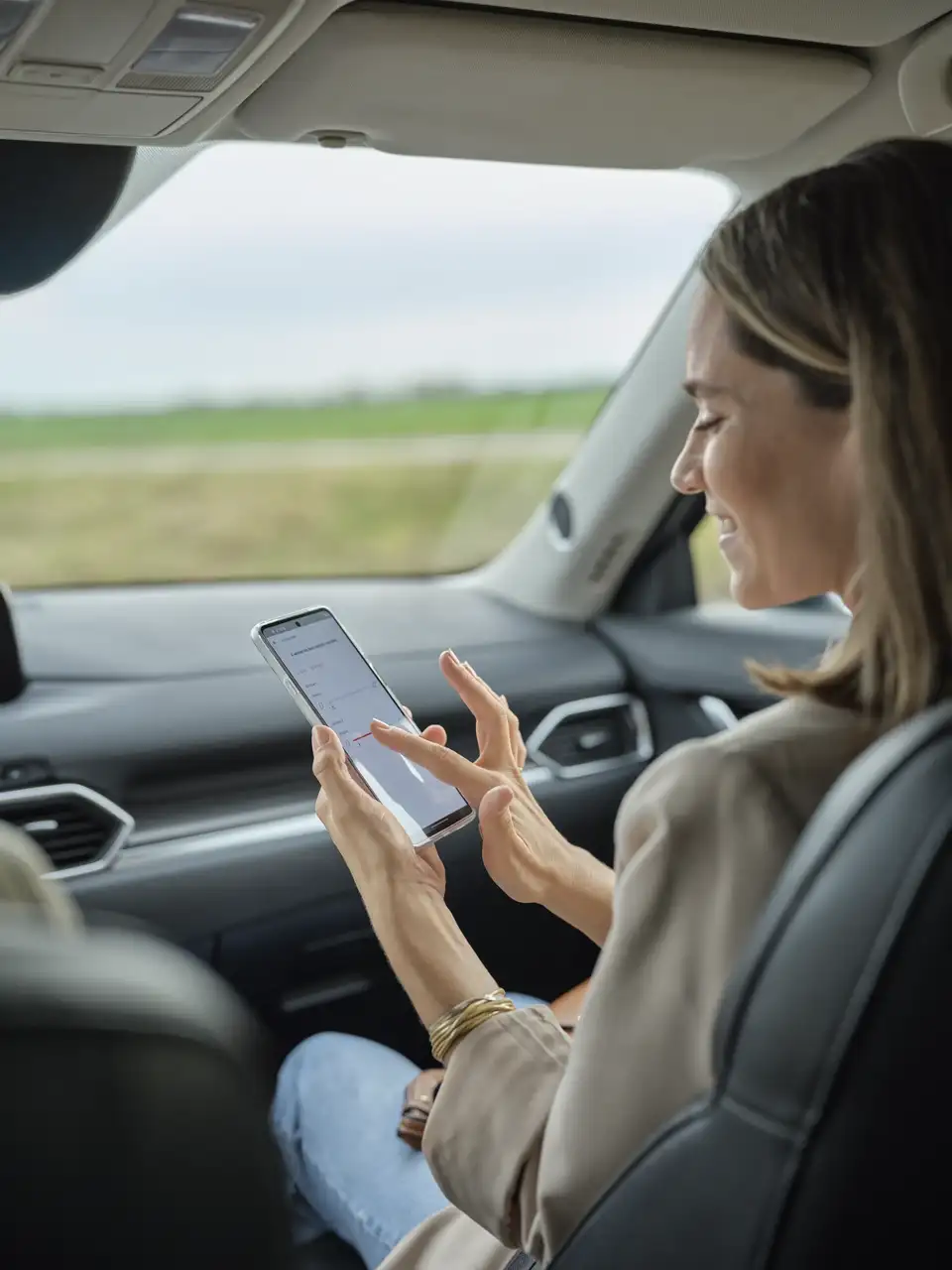 Arabada oturan bir kadın, VELUX App Control ile elektrikli çatı pencerelerini uzaktan kontrol ediyor