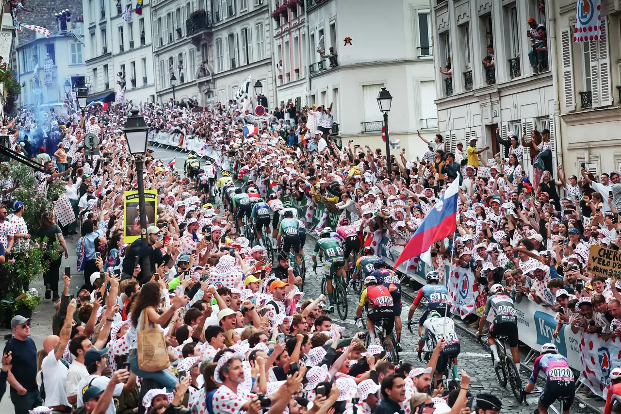 Kolesarji drvijo skozi mestne ulice, obdane z navijači na Tour de France.