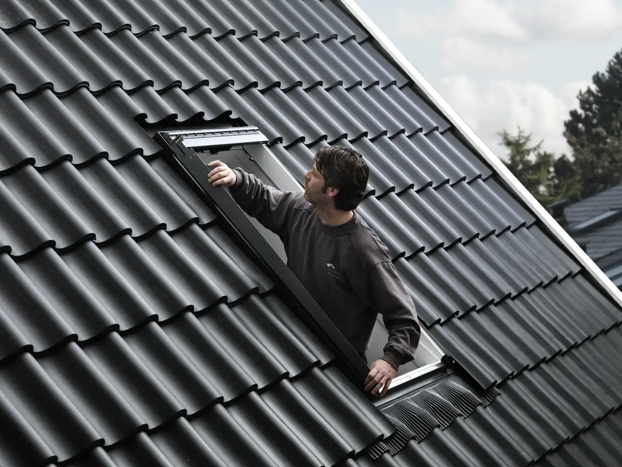 Un installateur règle une fenêtre de toit VELUX ouverte sur un toit en tuiles foncées
