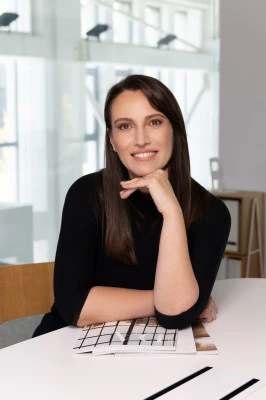 Woman smiling at a desk in a bright modern office with large windows behind her