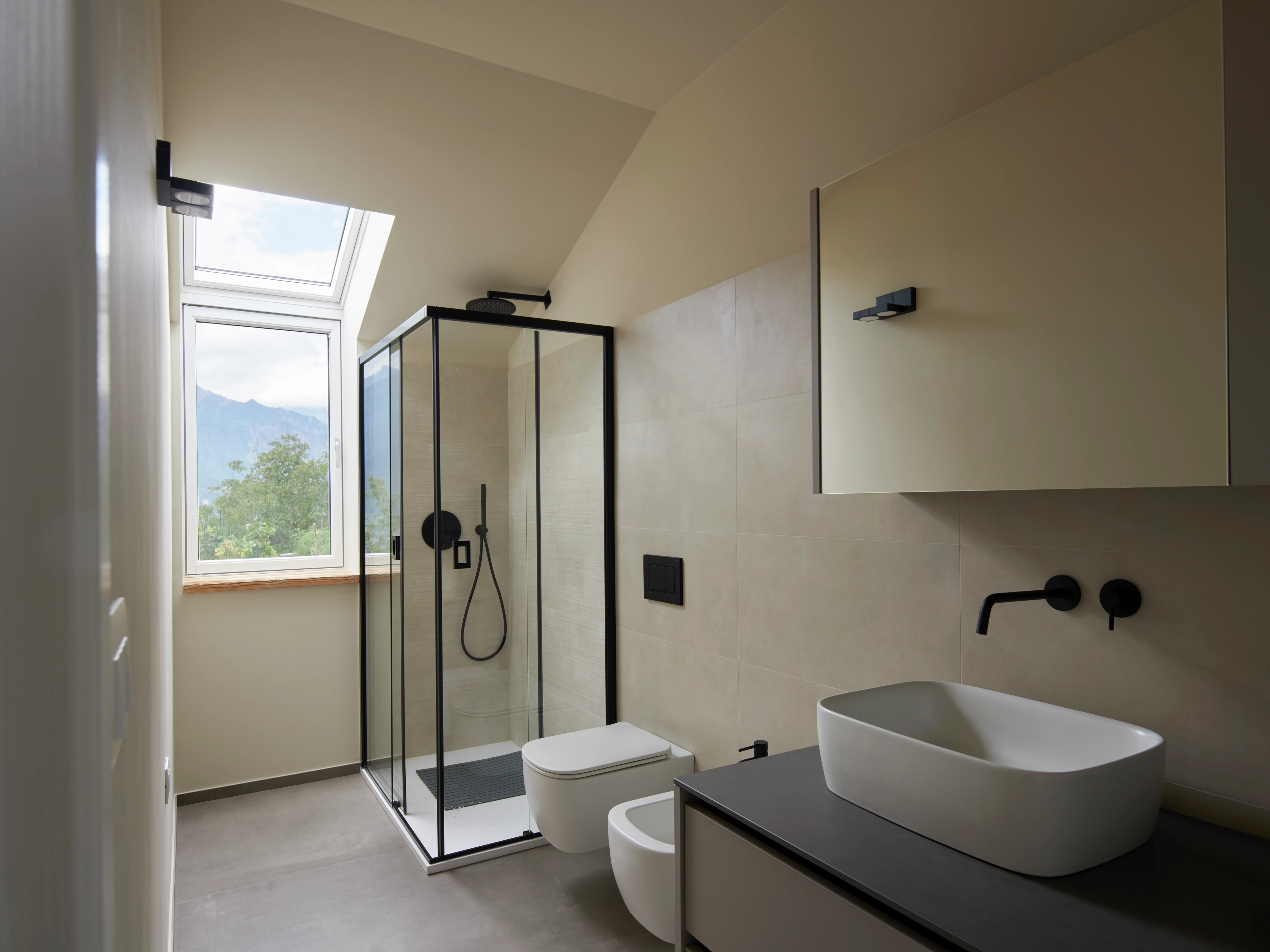 Bagno ristrutturato con soffitto inclinato, luce naturale e finestre VELUX con vista sulle montagne.