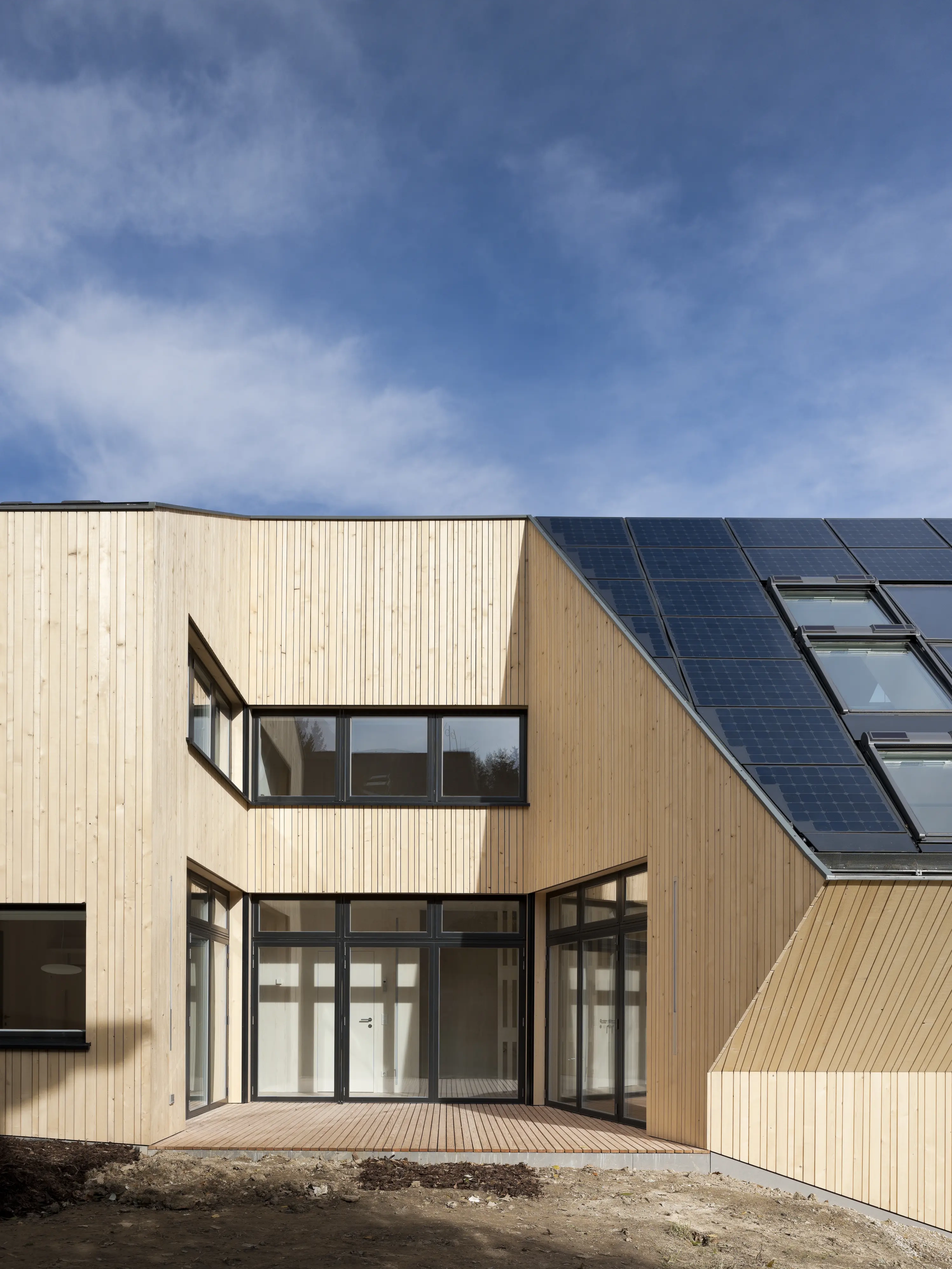 Wooden house with large windows and solar panels on the roof.
