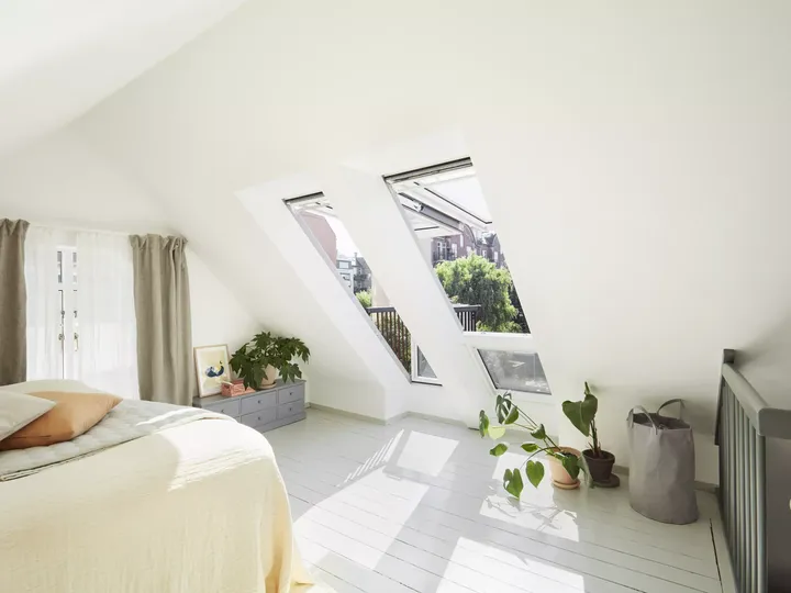 Schlafzimmer im Dachboden mit VELUX Dachflächenfenstern und weißer Dekoration.
