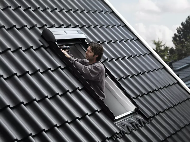 Handwerker steht in einer Dachluke, um ein Dachfenster zu montieren | VELUX Magazin