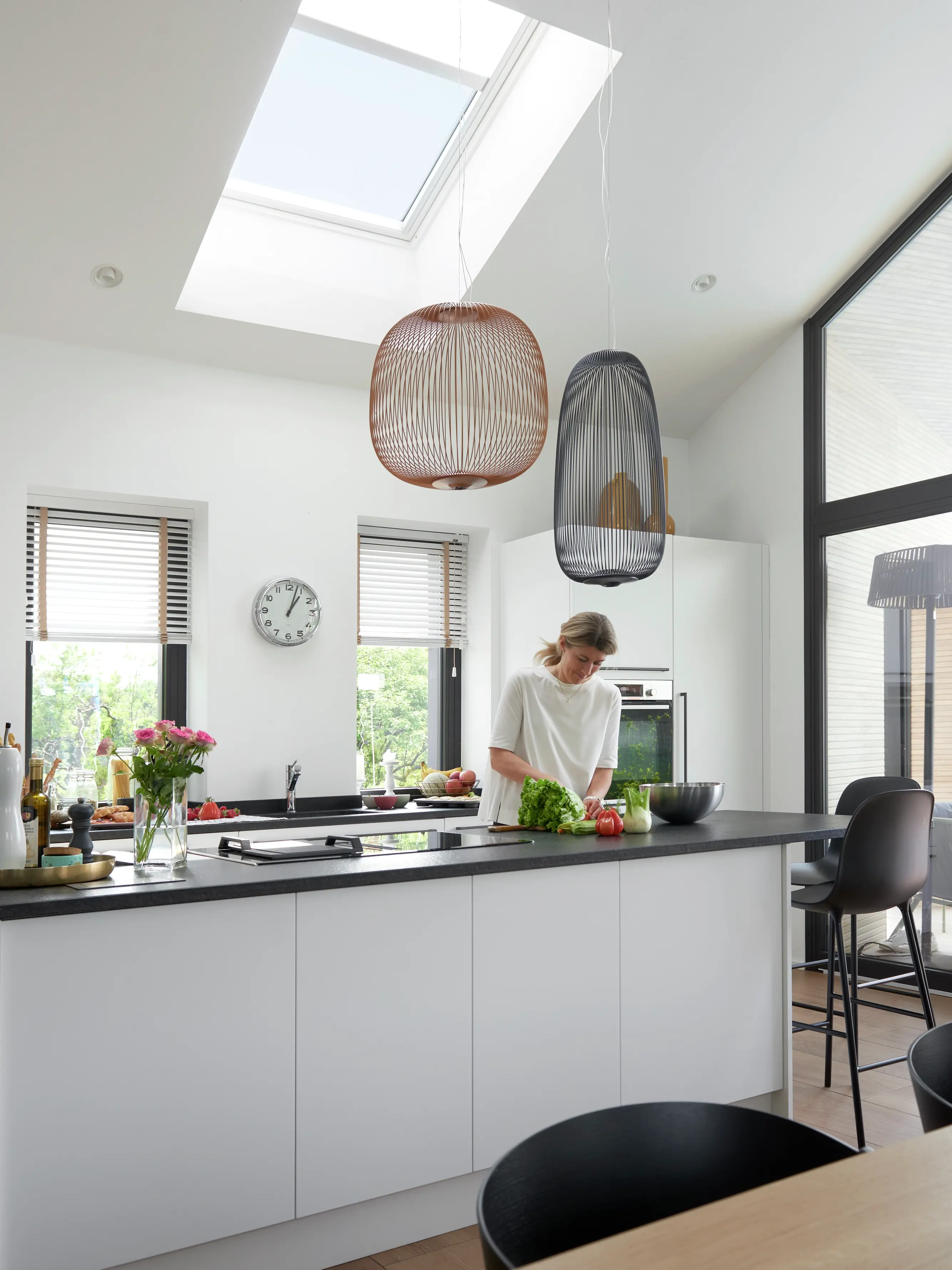 Cucina moderna con mobili bianchi, piano di lavoro nero e una finestra per tetti VELUX.