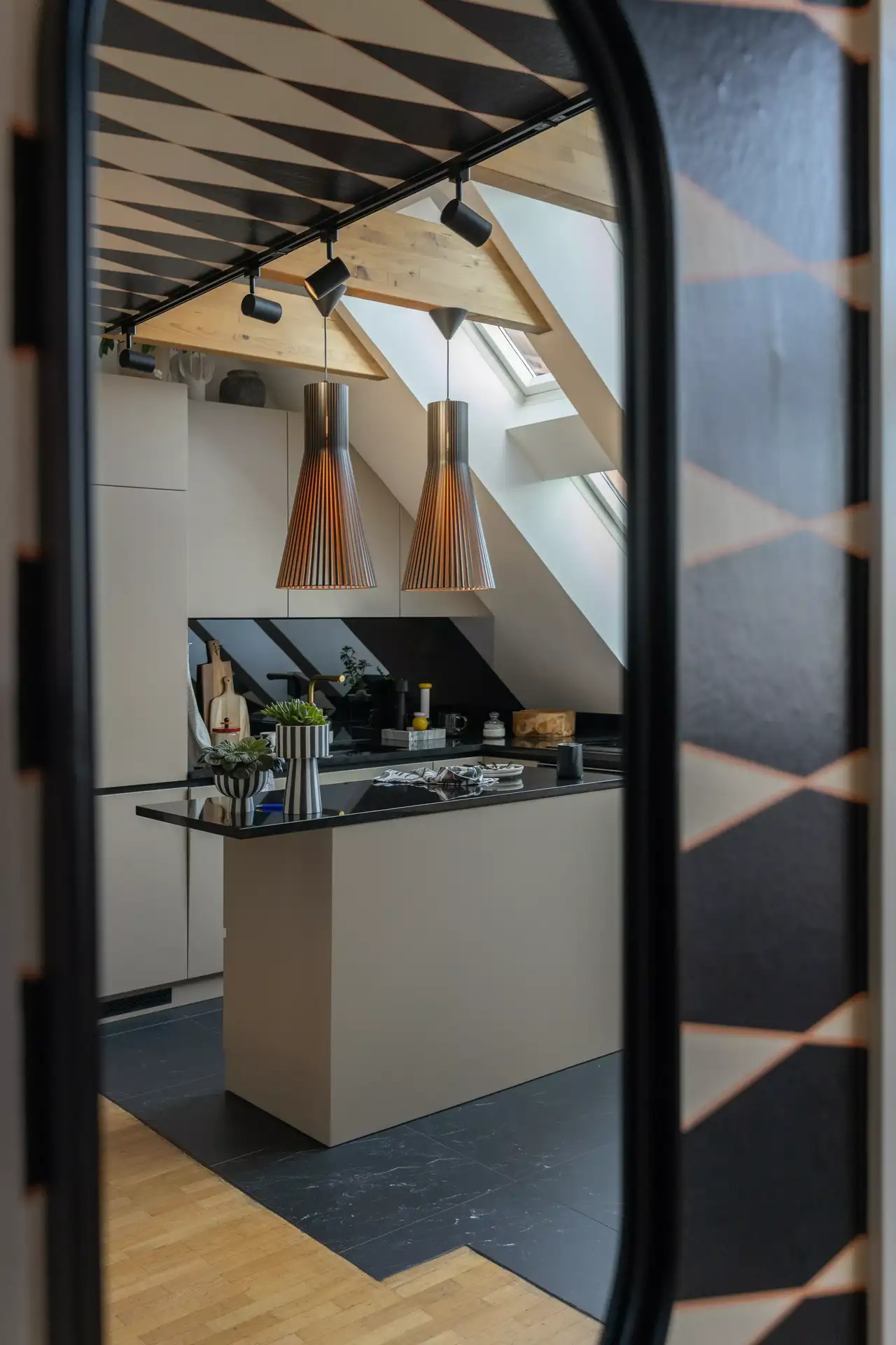 Moderne Küche mit zentraler Insel, beleuchtet durch VELUX Fenster, kontrastreiche Töne und Hängebeleuchtung.