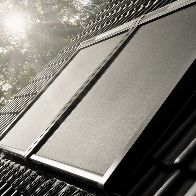 Roof with solar panels and black tiles, sunlight filtering through trees.