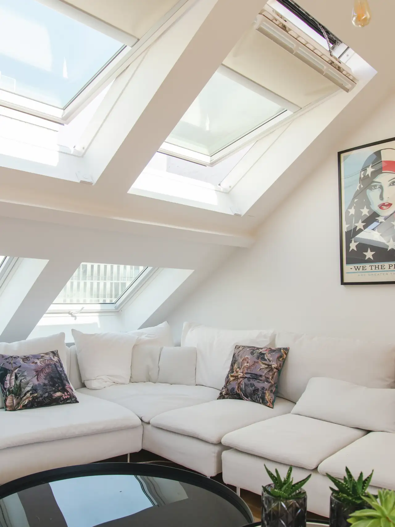 Een binnenruimte met een schuin plafond met twee dakramen. Onder de dakramen is er een ingebouwde zithoek met kussens en sierkussens. De kamer is licht dankzij het natuurlijke licht dat door de dakramen naar binnen valt.