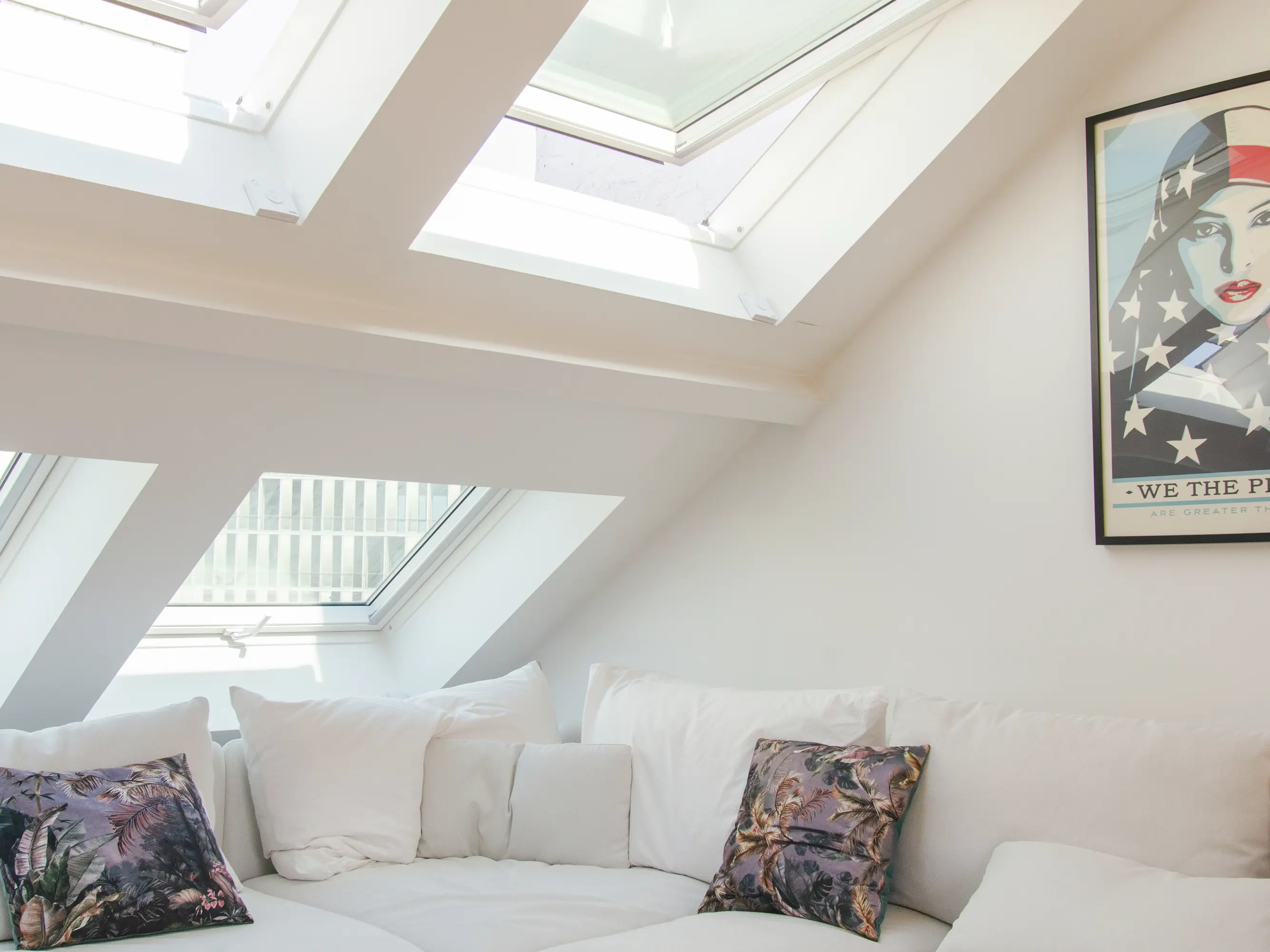 Salon de comble confortable avec lumière naturelle provenant des fenêtres de toit VELUX et un canapé blanc moelleux.