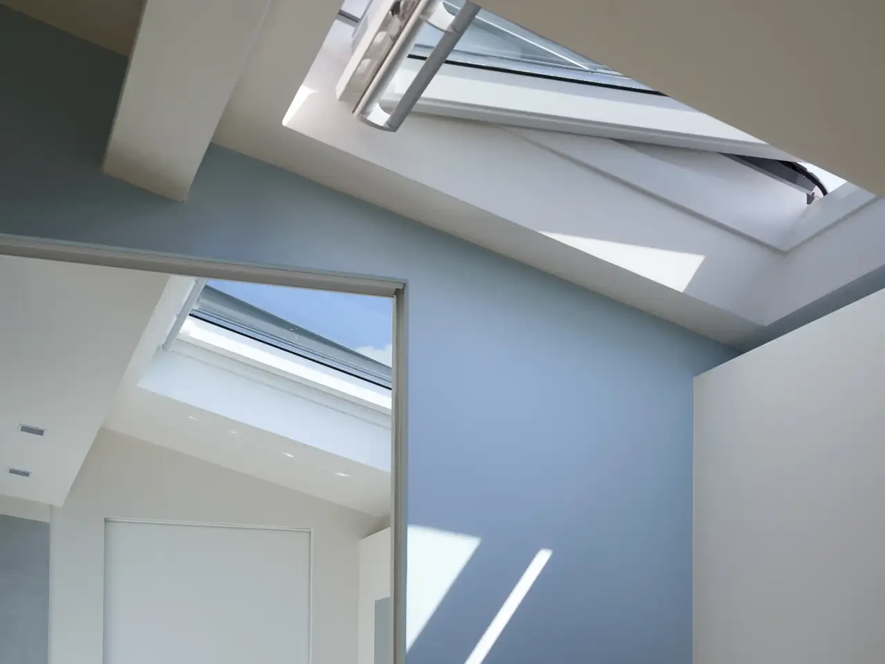 Grande specchio davanti a una parete blu sotto un lucernario aperto | Rivista VELUX