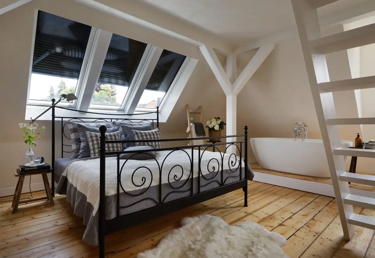 Un dormitorio con la cama colocada bajo las ventanas de tejado, con persianas medio cerradas.