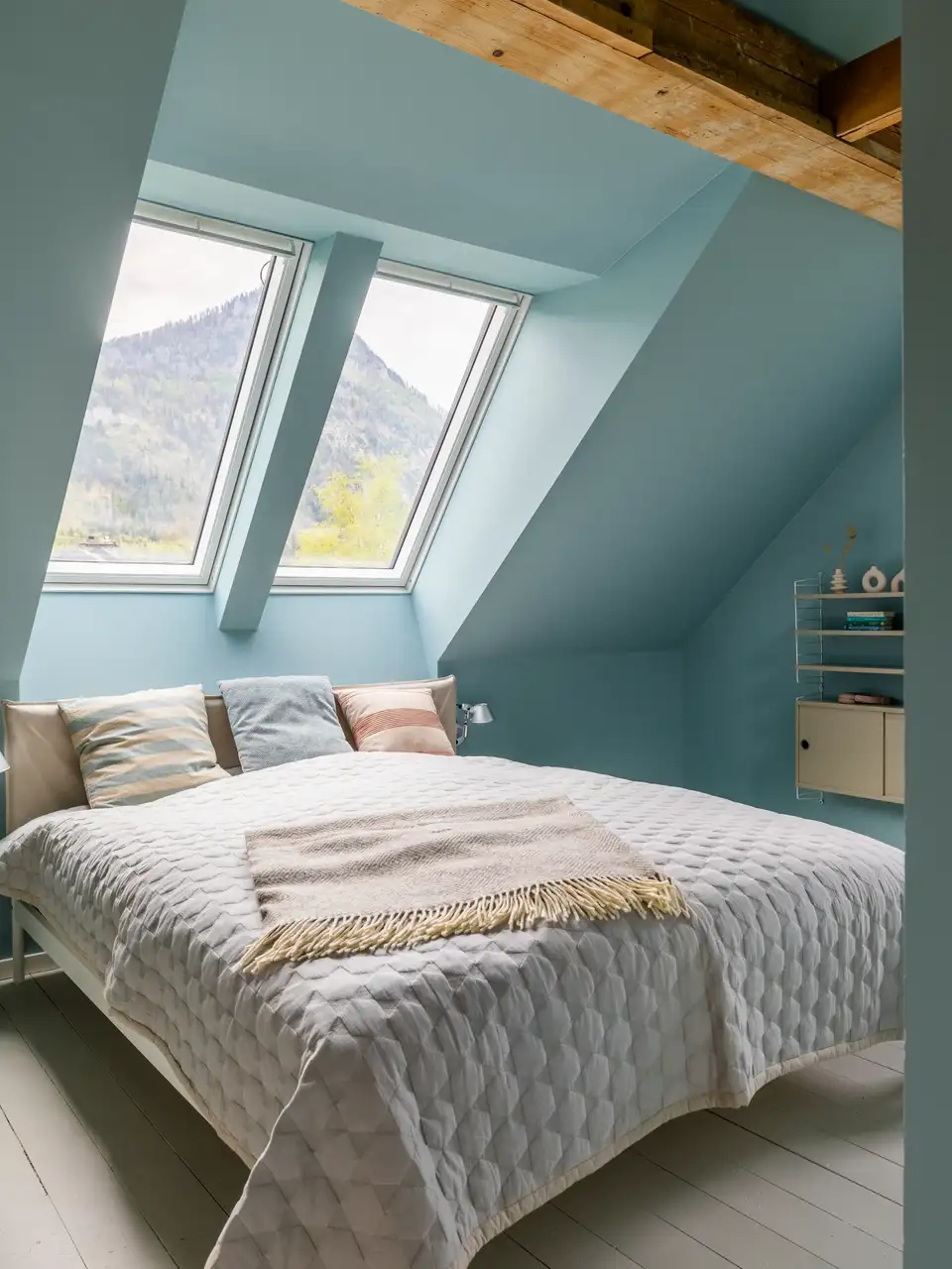 Camera da letto mansardata con travi in legno e due finestre per tetti.