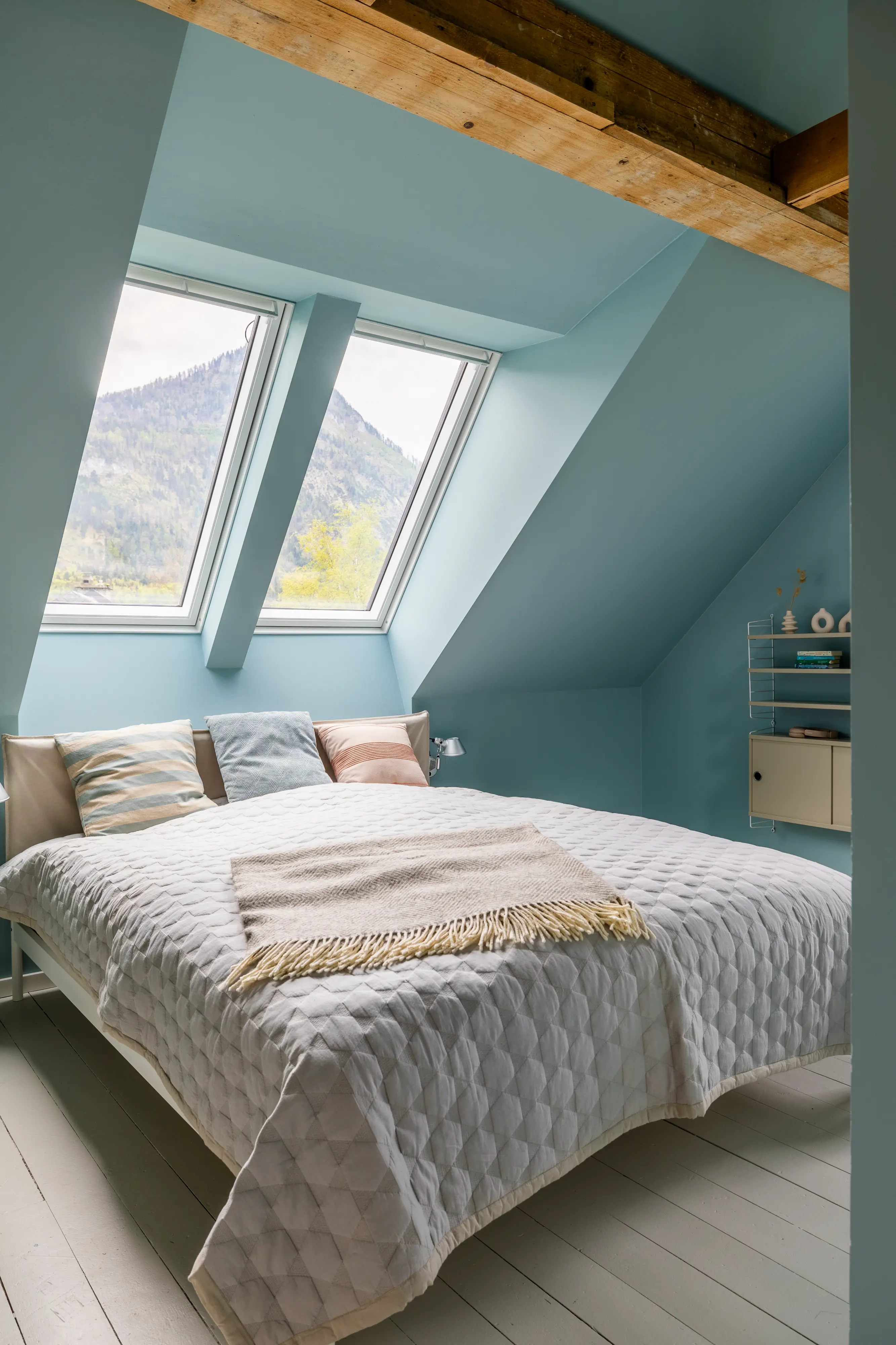 Palėpės miegamasis su nuožulniomis lubomis ir VELUX stogo langais, vaizdu į kalnus.