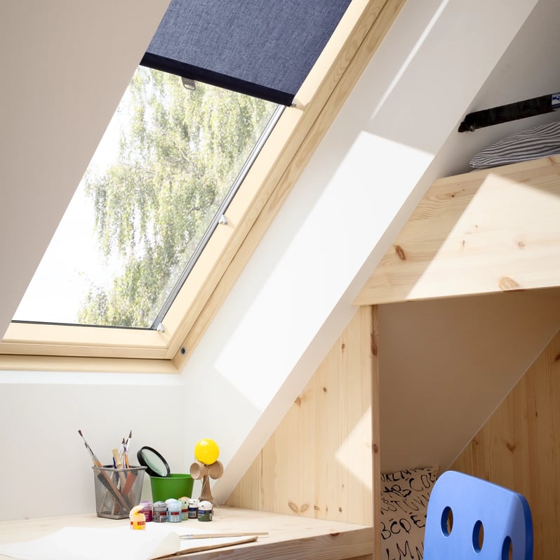 Attic workspace with sloped ceiling and VELUX roof window, art supplies on desk.