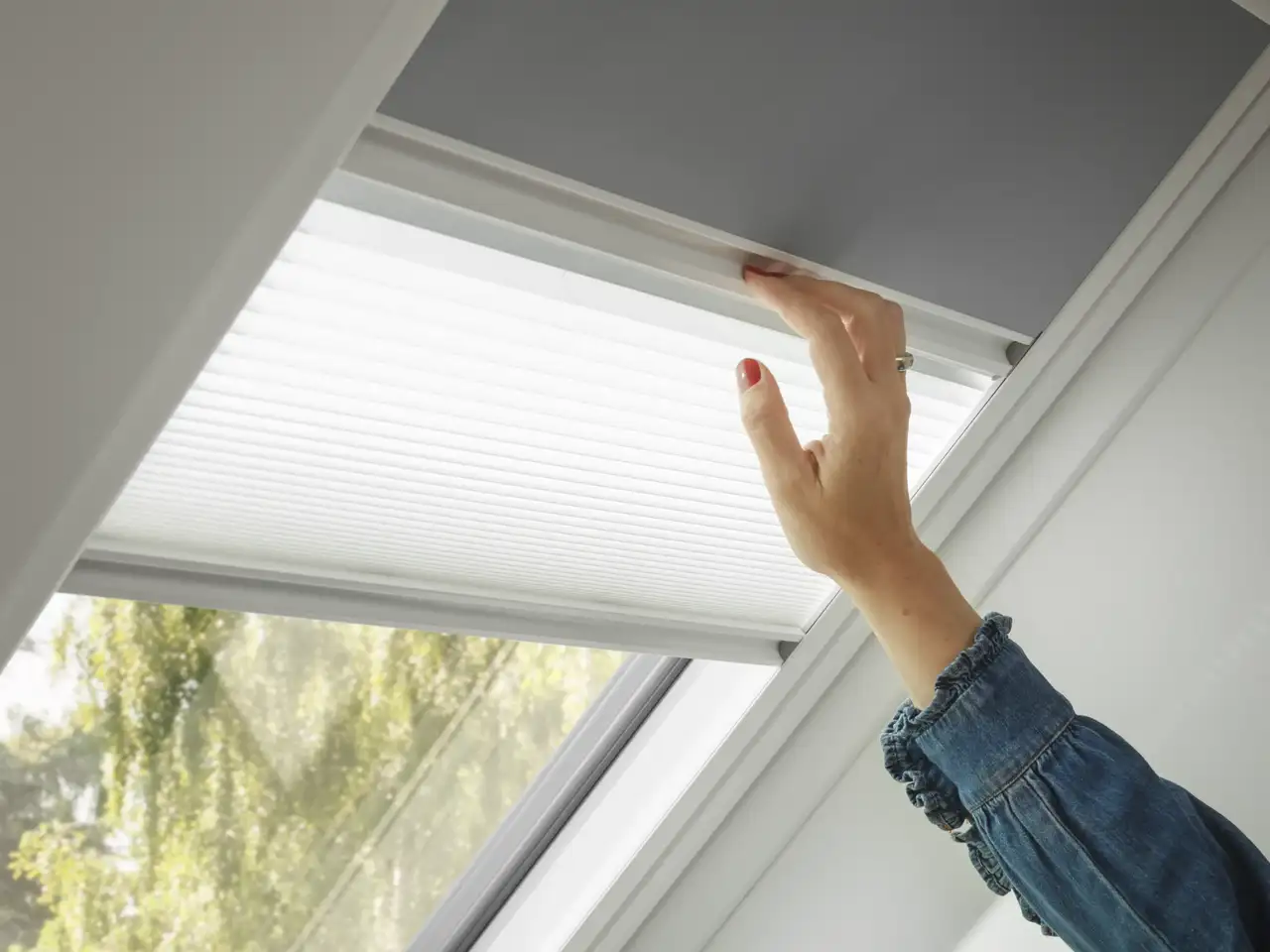 main ajustant un store sur une fenêtre de toit VELUX, lumière naturelle filtrée     