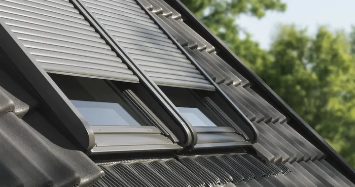 Bližnji posnetek zunanjih rolet VELUX, nameščenih na poševni strehi, ki zagotavljajo toplotno izolacijo in zaščito pred soncem.
