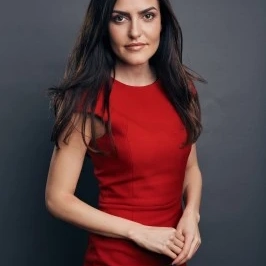 Woman in a red dress standing against a dark background, looking confidently at the camera.