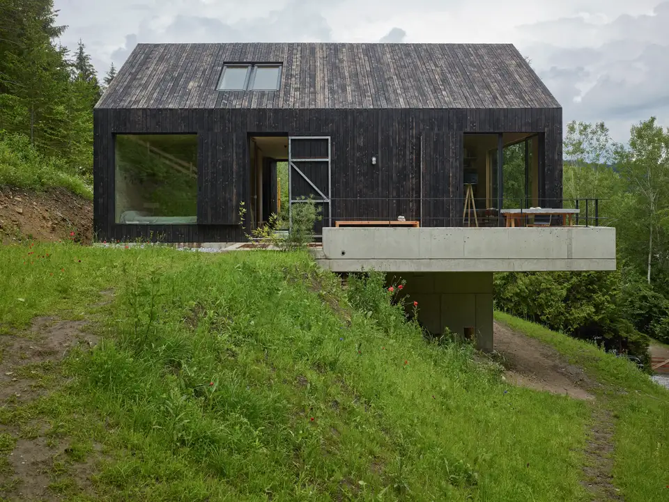 Casa con tetto a falde su una collina con grandi aperture verticali in vetro e due finestre per tetti.