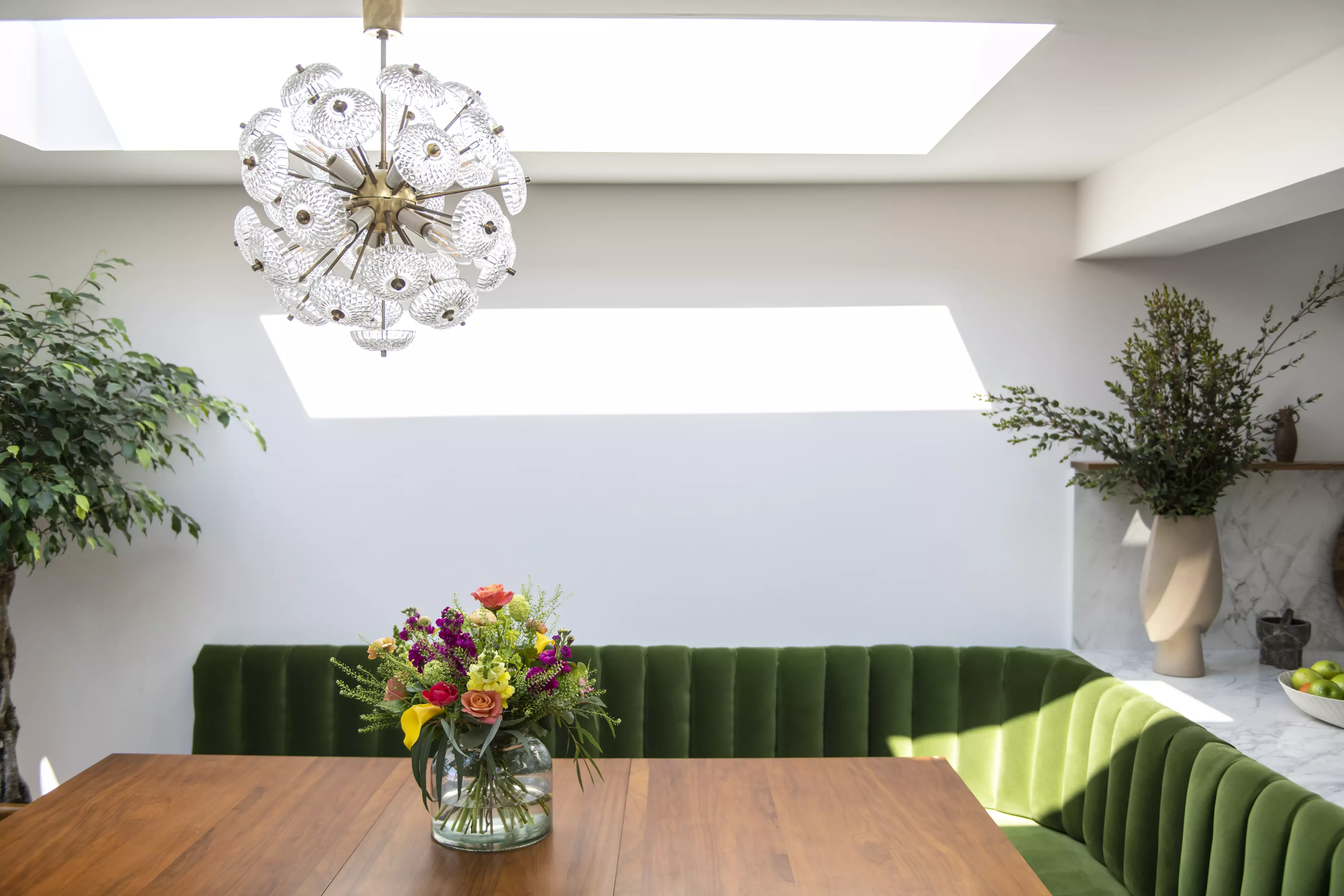 Chic dining room with VELUX windows, green banquette, and a chandelier.