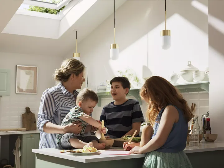 Familie kocht gemeinsam in einer sonnendurchfluteten Küche mit einem VELUX Dachflächenfenster.