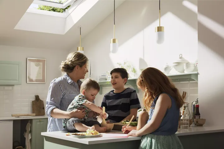 Familie kocht gemeinsam in einer hellen Küche mit einem VELUX Dachflächenfenster.