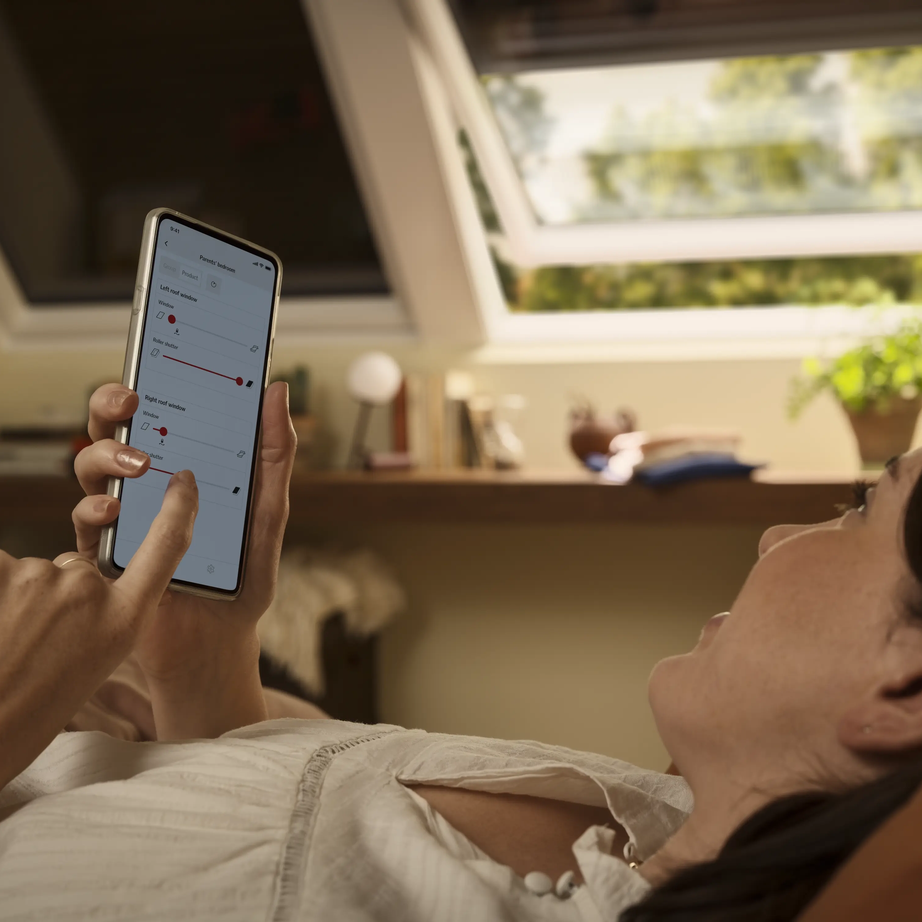 Attic room with VELUX roof window, woman using smart phone for remote control.