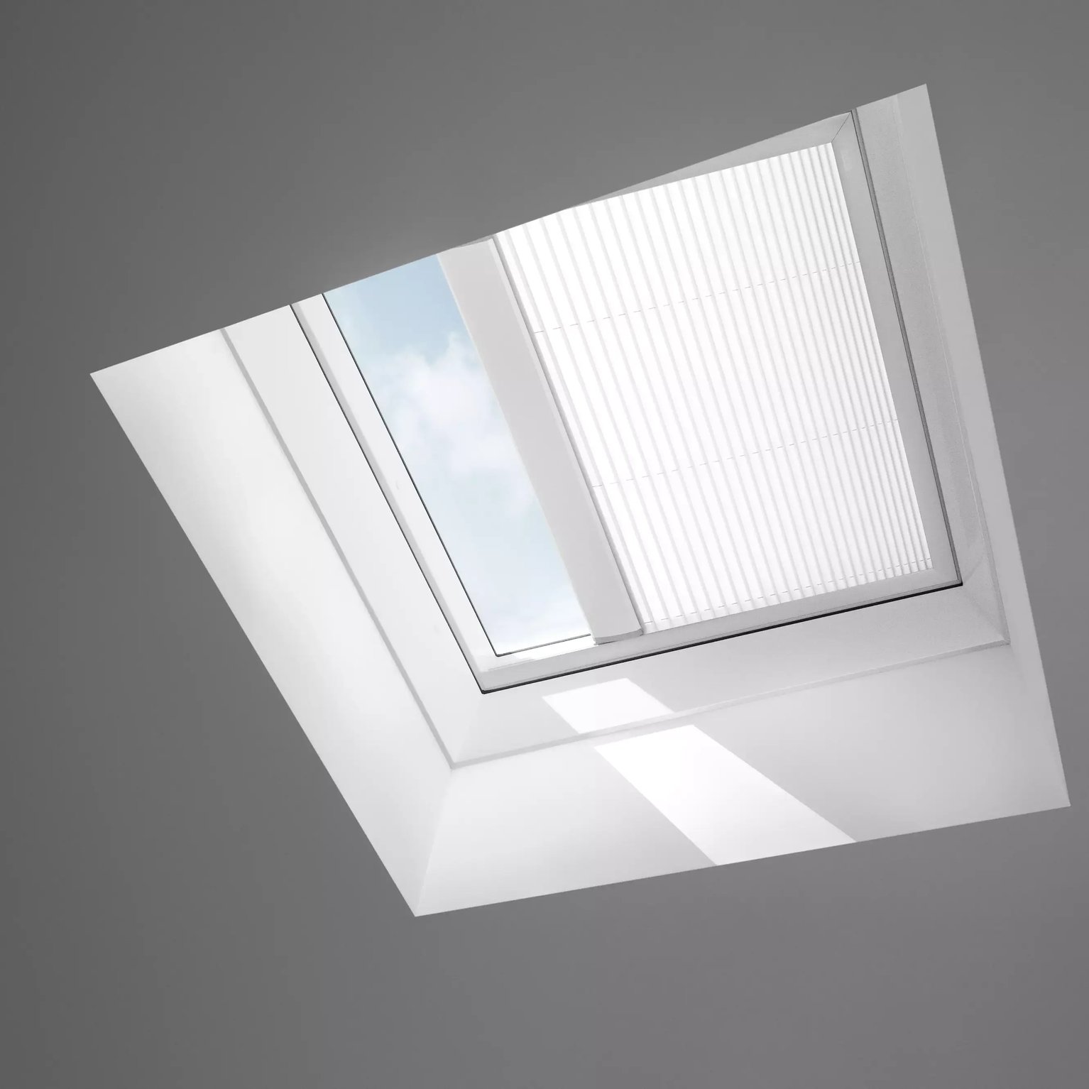 Closed VELUX roof window in a sloped ceiling, view of sky and clouds.