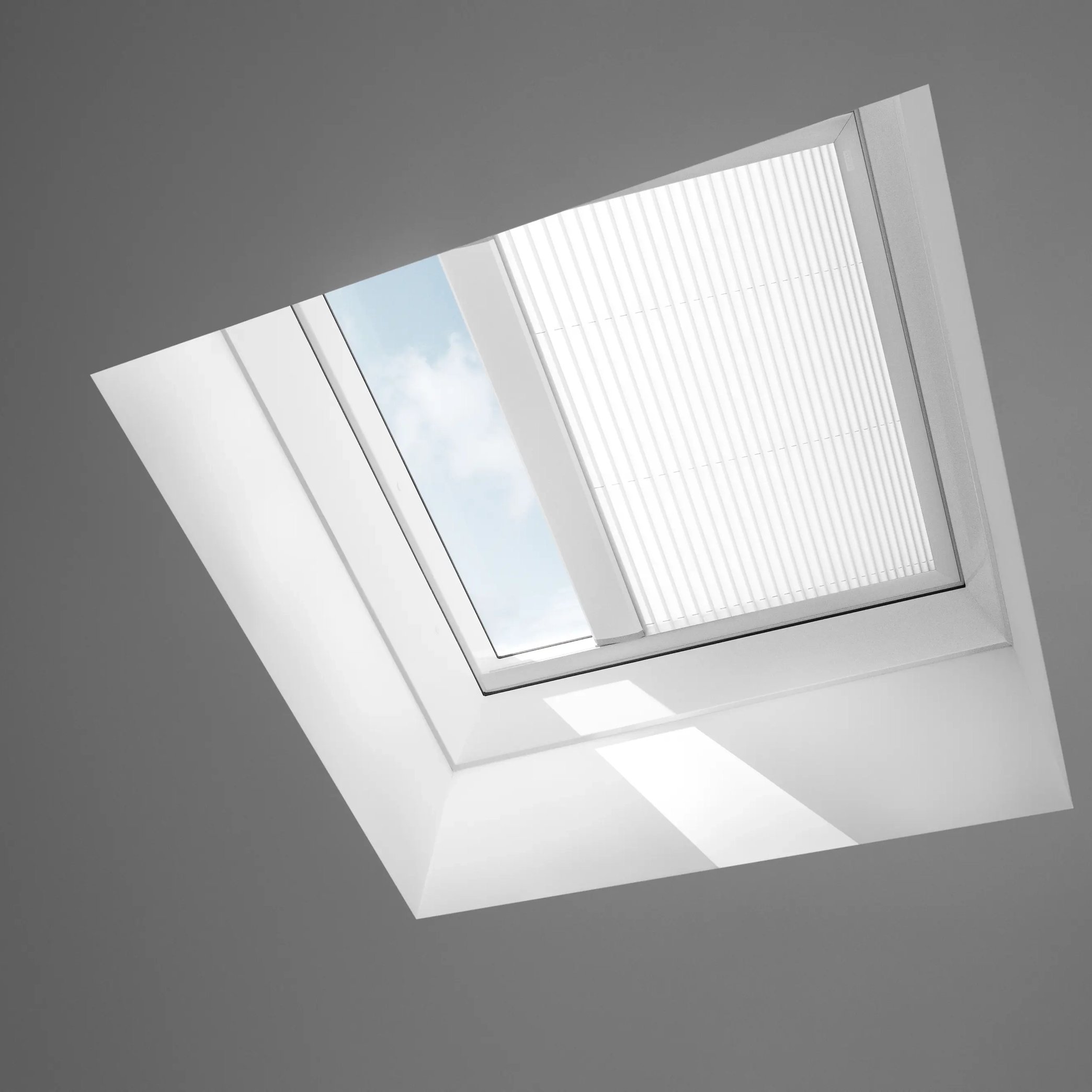 Closed VELUX roof window in a sloped ceiling, view of sky and clouds.