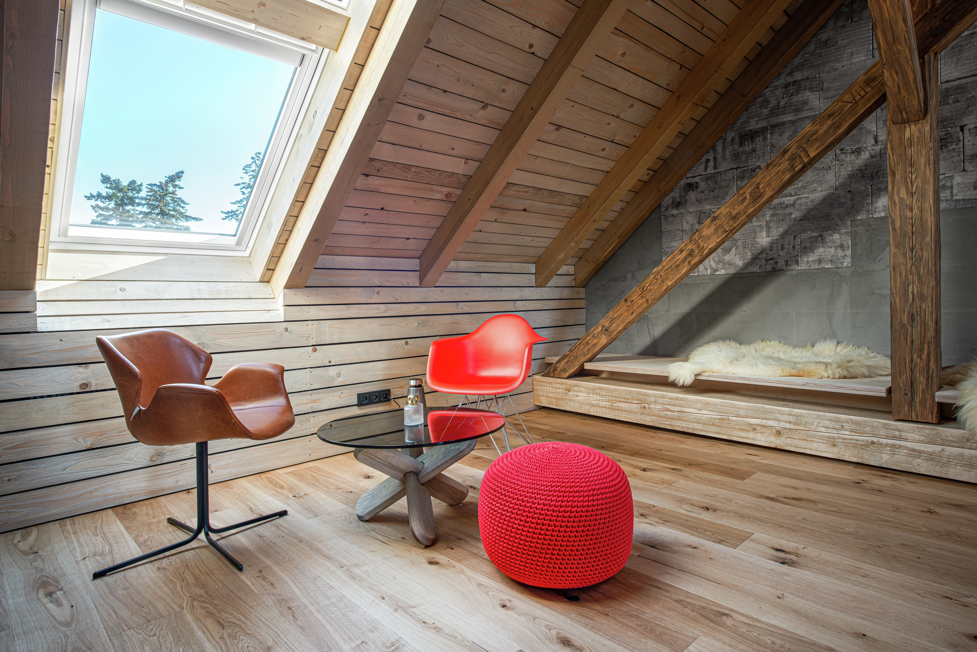 Attic lounge with sloped ceiling, VELUX window, modern furniture, and wooden rafters.