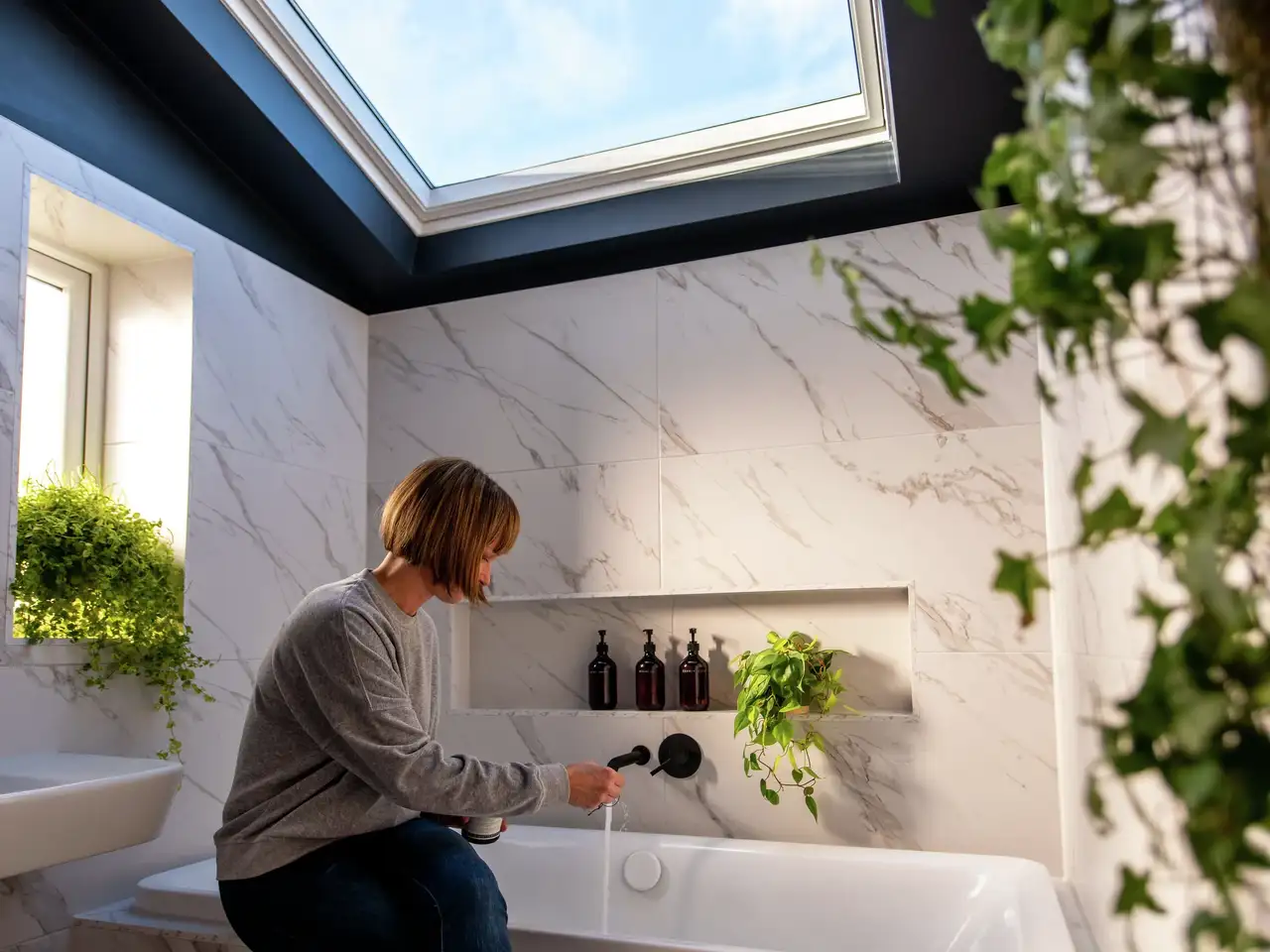 Modern bathroom with VELUX roof window, marble tiles, and greenery.