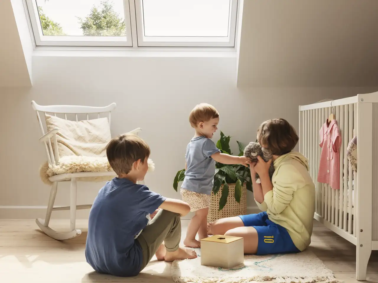 Trois enfants jouent dans la chambre de bébé sous la fenêtre de toit devant une plante purificatrice d'air | Magazine VELUX