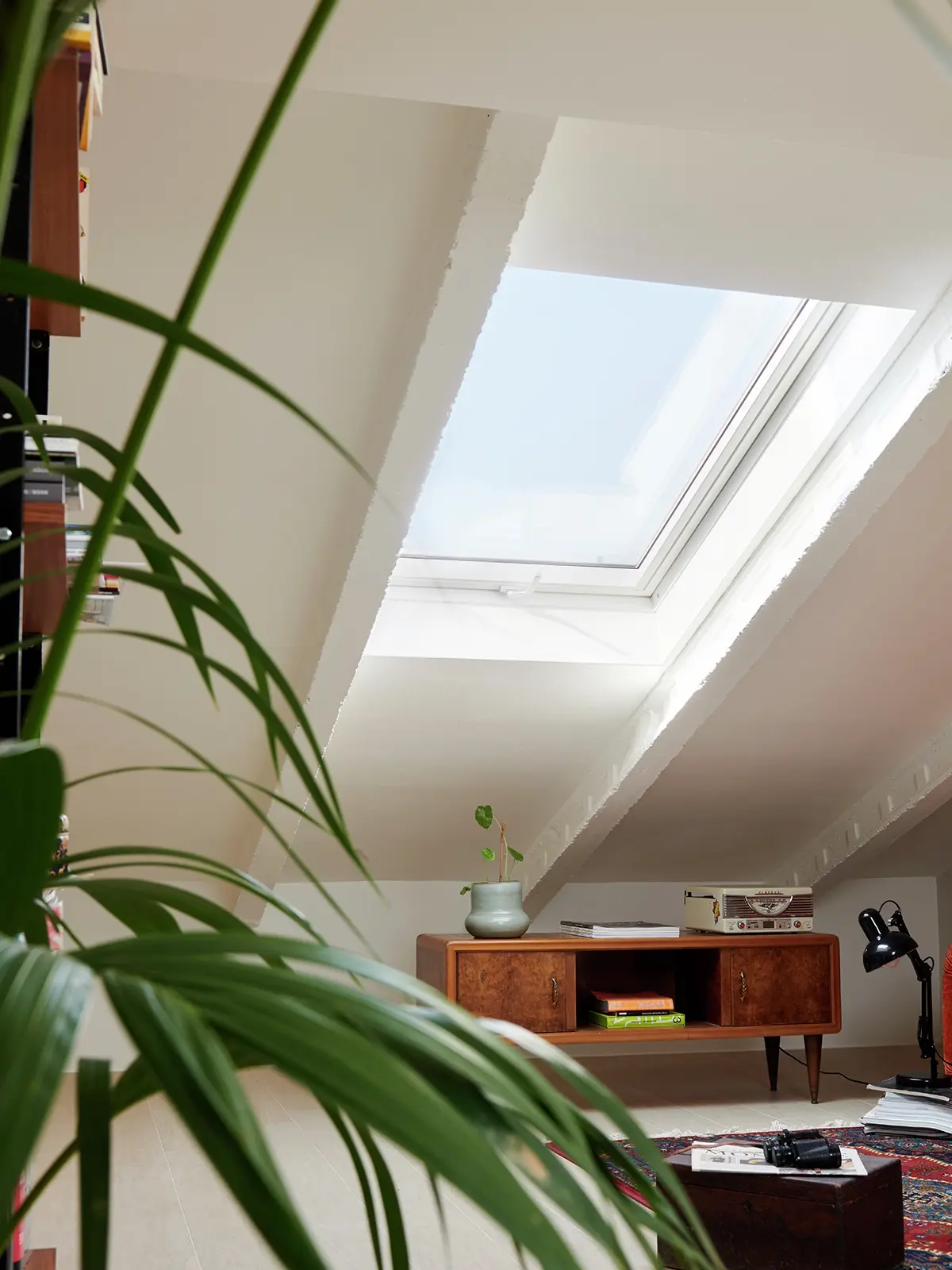 Bureau à domicile confortable sous les combles avec lumière naturelle provenant d'une fenêtre de toit VELUX, bureau vintage et plantes.