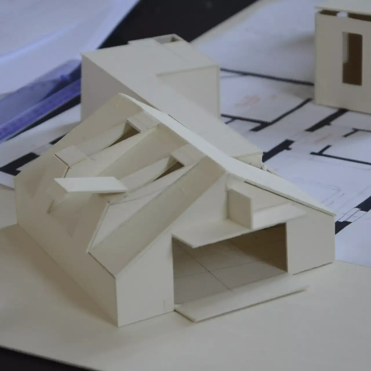 Architekturmodell eines modernen Gebäudes mit Entwurfsplänen im Hintergrund.