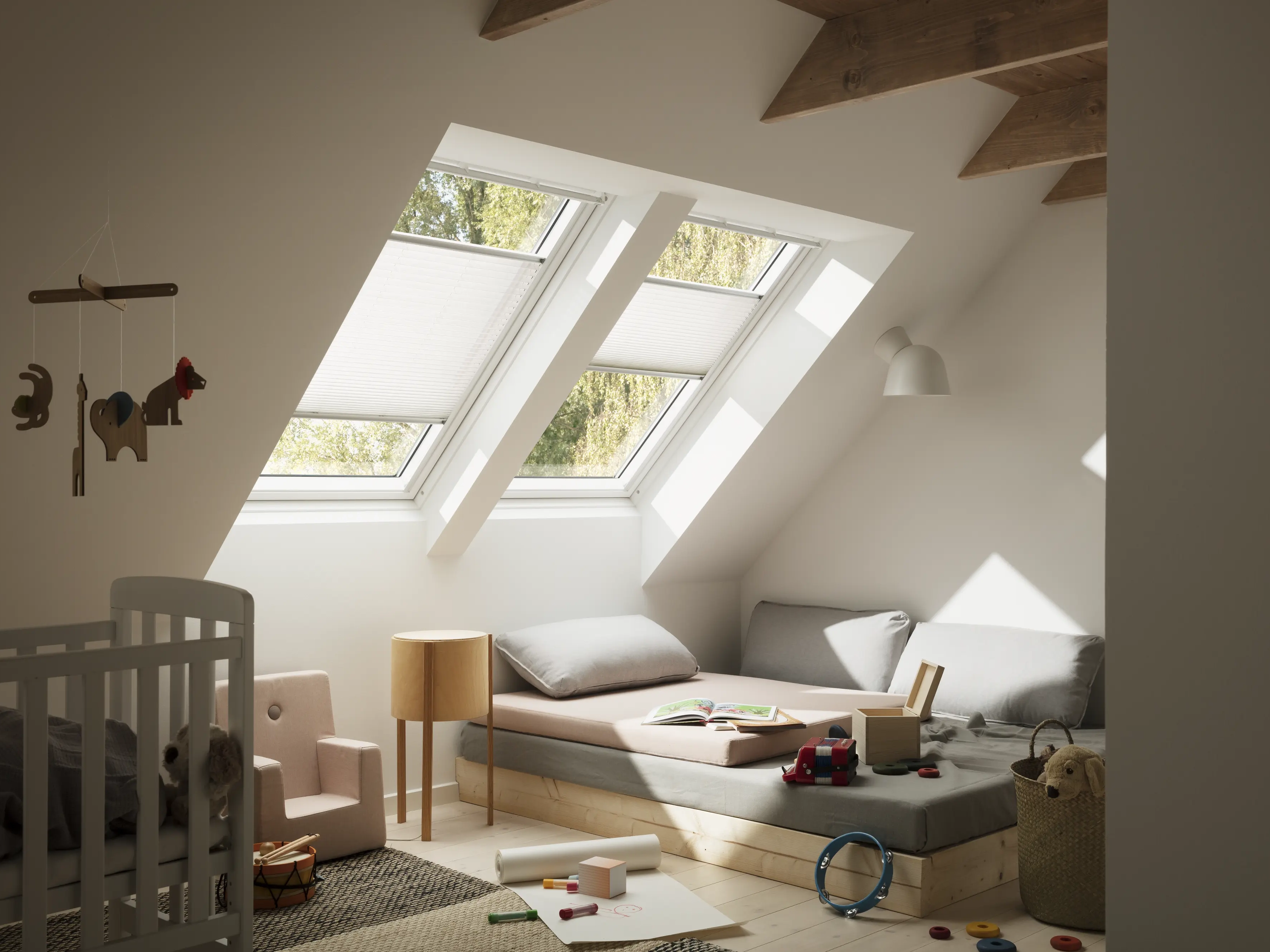 chambre d'enfant sous combles avec deux fenêtres de toit VELUX équipées de stores tamisants, berceau et jouets au sol