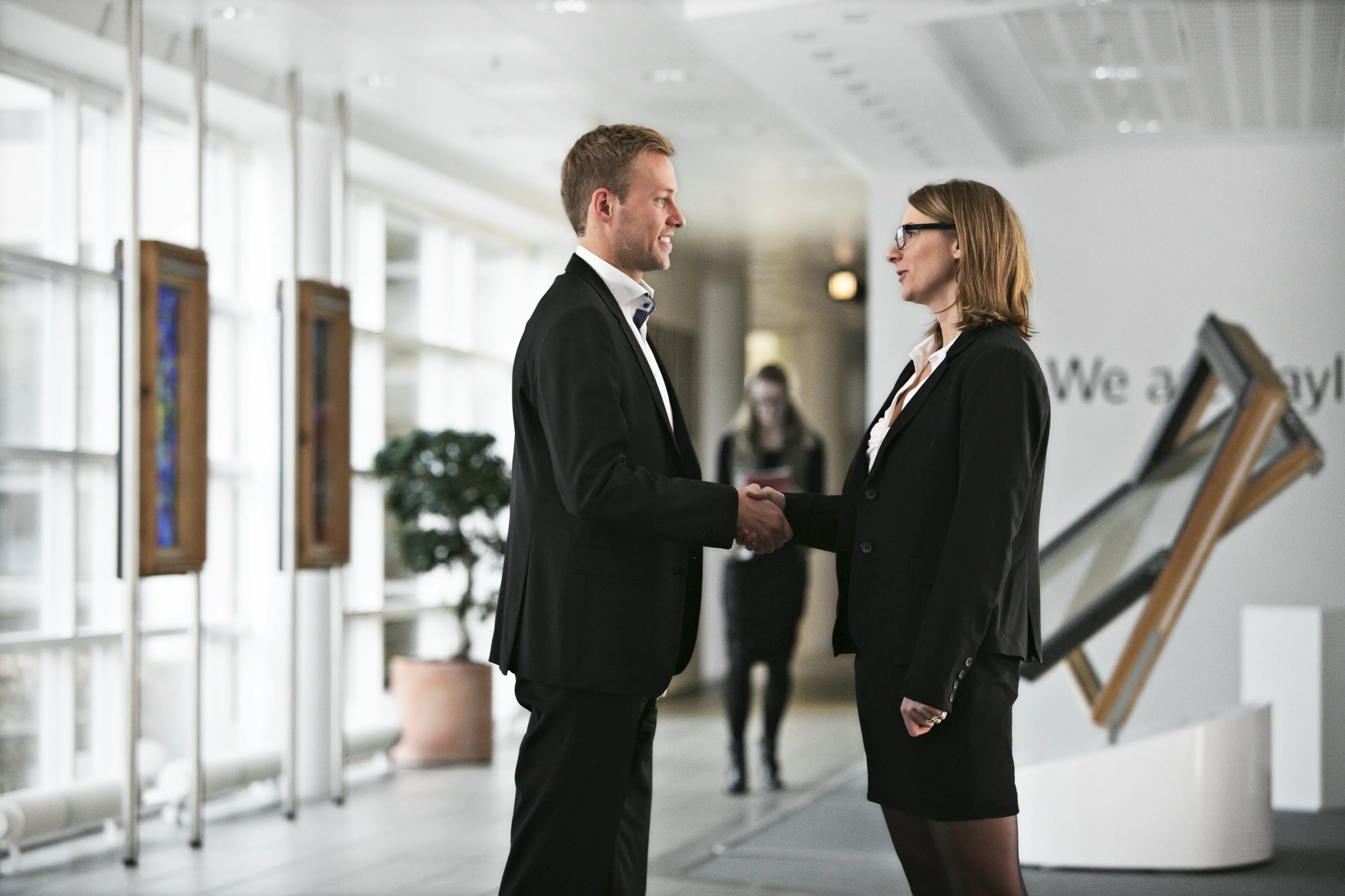 Two professionals shaking hands in a modern office with large windows.