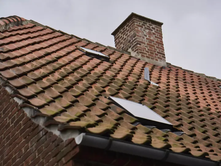 Nahaufnahme eines VELUX Dachflächenfensters auf einem terrakottafarbenen Ziegeldach mit einem gemauerten Schornstein.