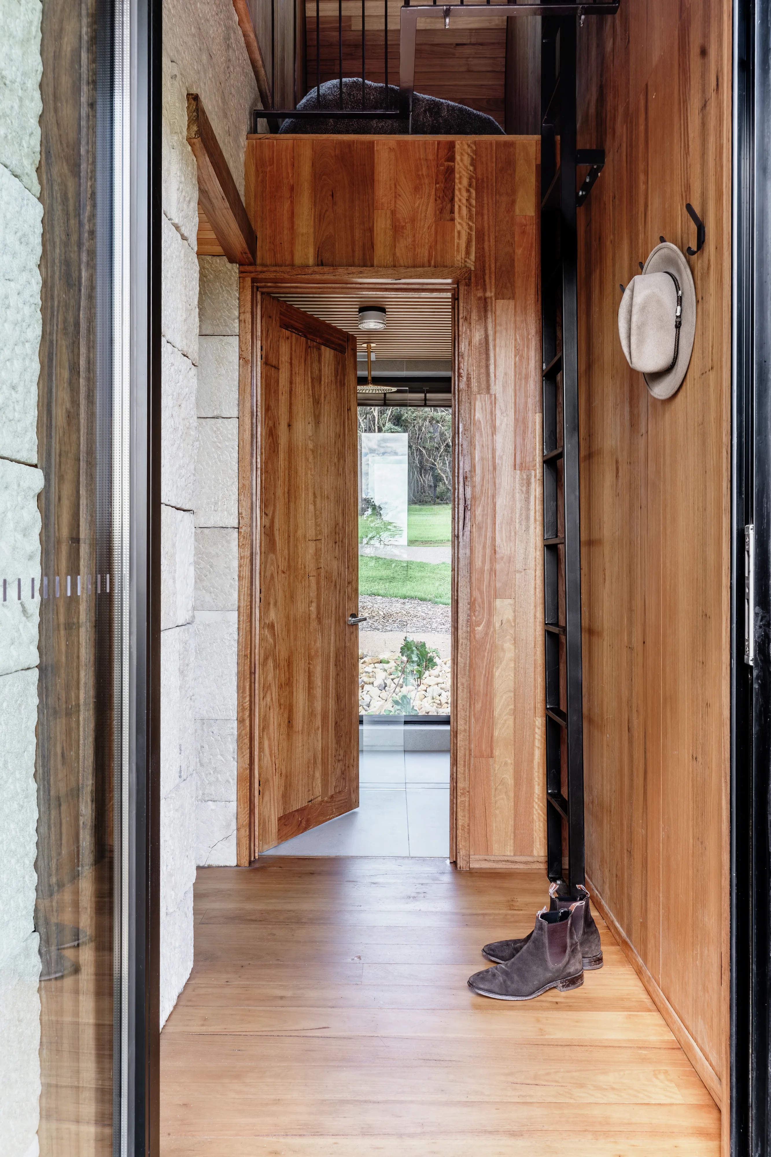 Wooden hallway with boots by the wall leading to a bright room and garden view.