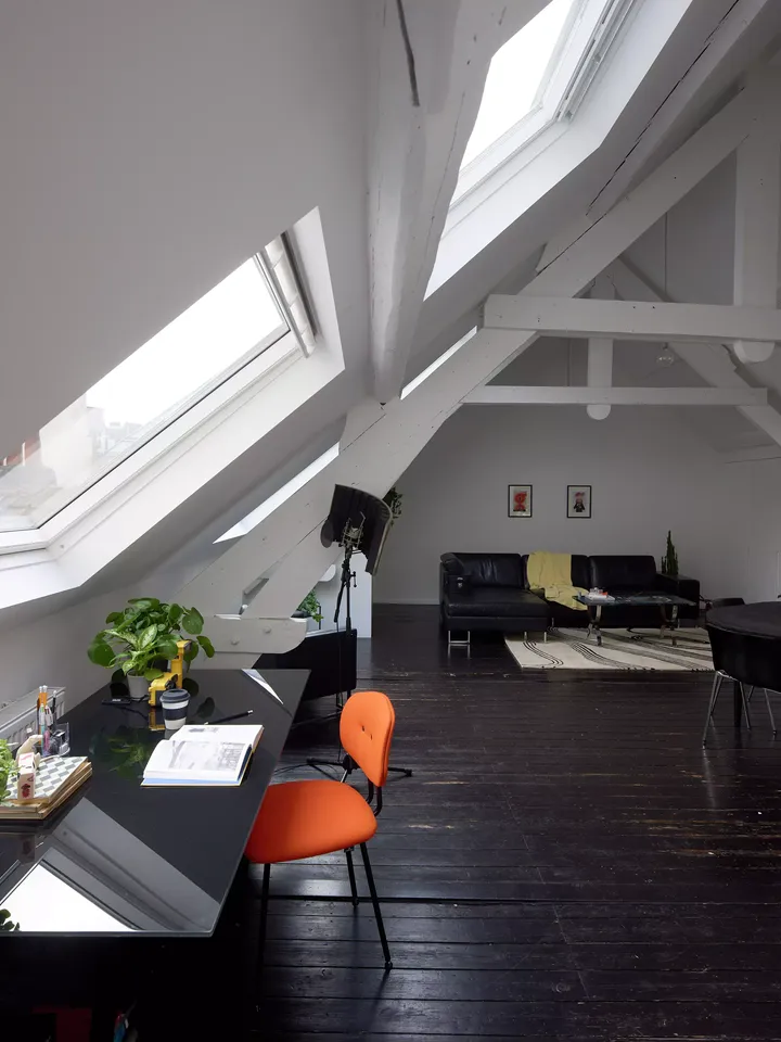 Ausgebauter Spitzboden mit weißen Wänden, schwarzem Boden und Dachfenstern dient als Arbeitszimmer und Lounge im Dachgeschoss | VELUX Magazin