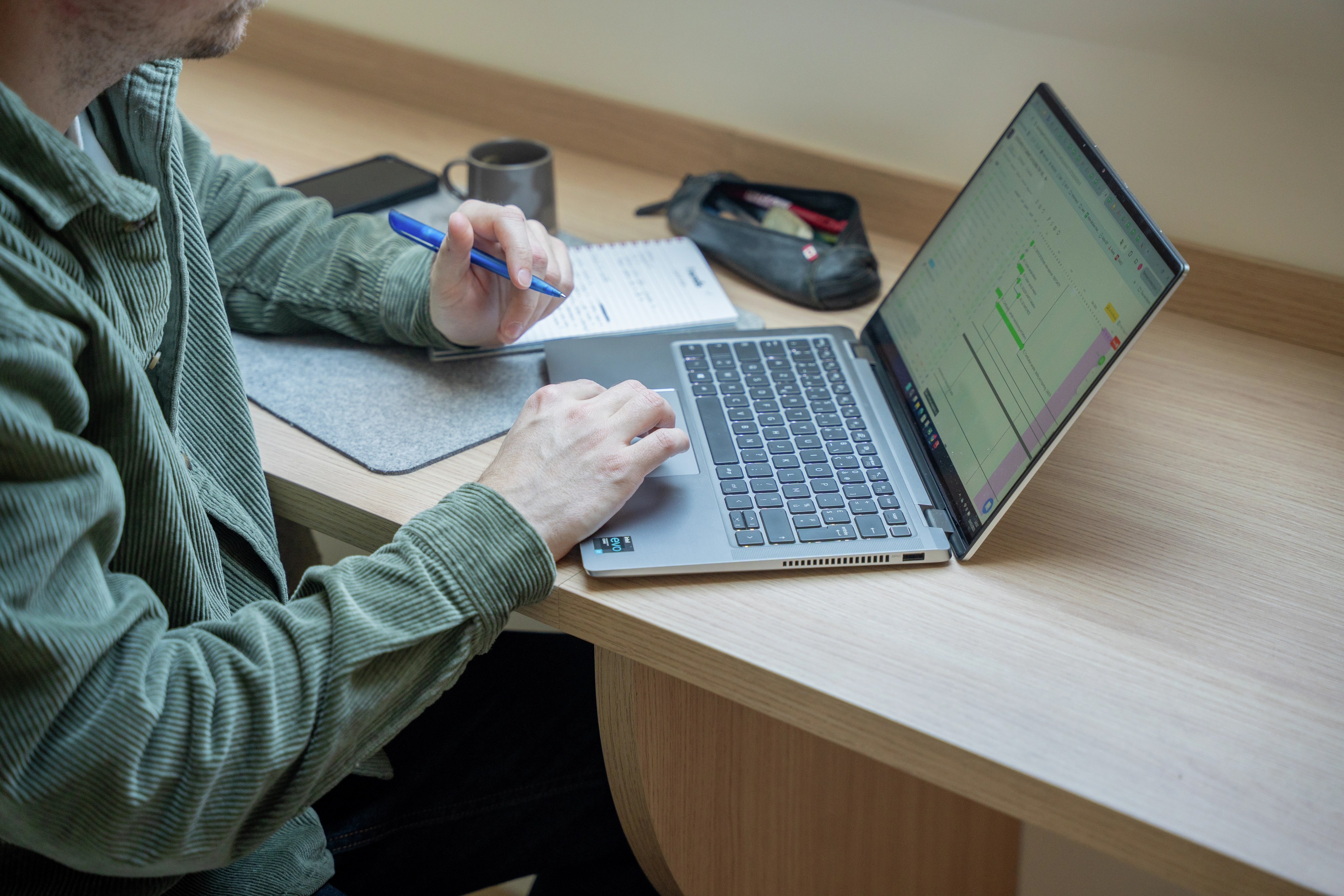Person working at home office desk with laptop and notebook.