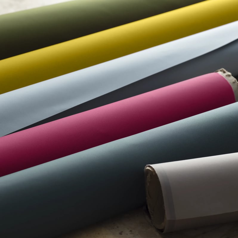 Vibrant fabric rolls in green, yellow, pink, and blue, neatly arranged.