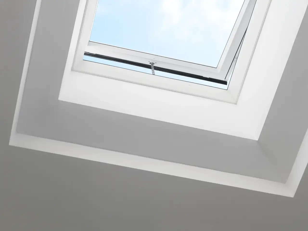 Finestra per tetti piani VELUX aperta con vista chiara del cielo e delle nuvole.