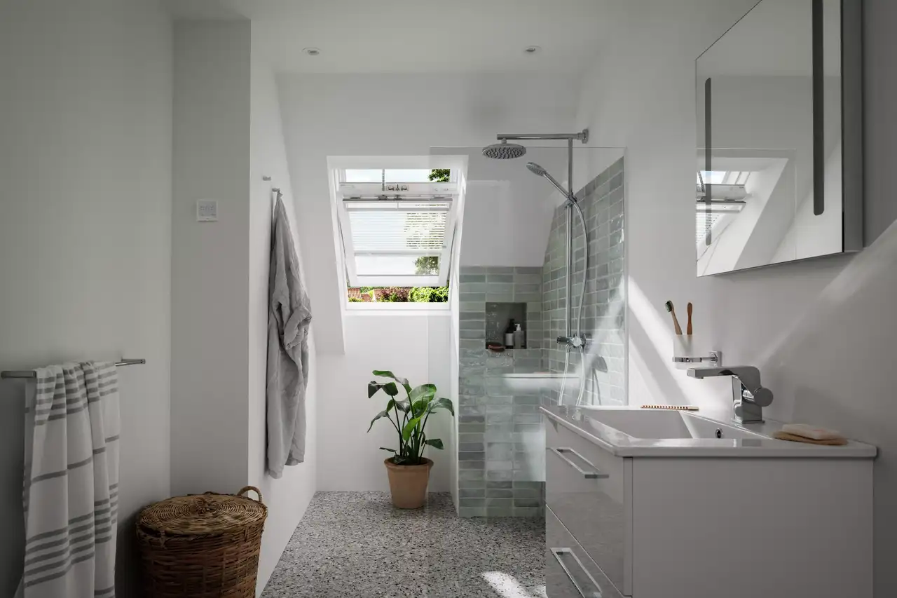 Bagno mansardato con lavandino e doccia e finestra per tetti VELUX con tende alla veneziana.