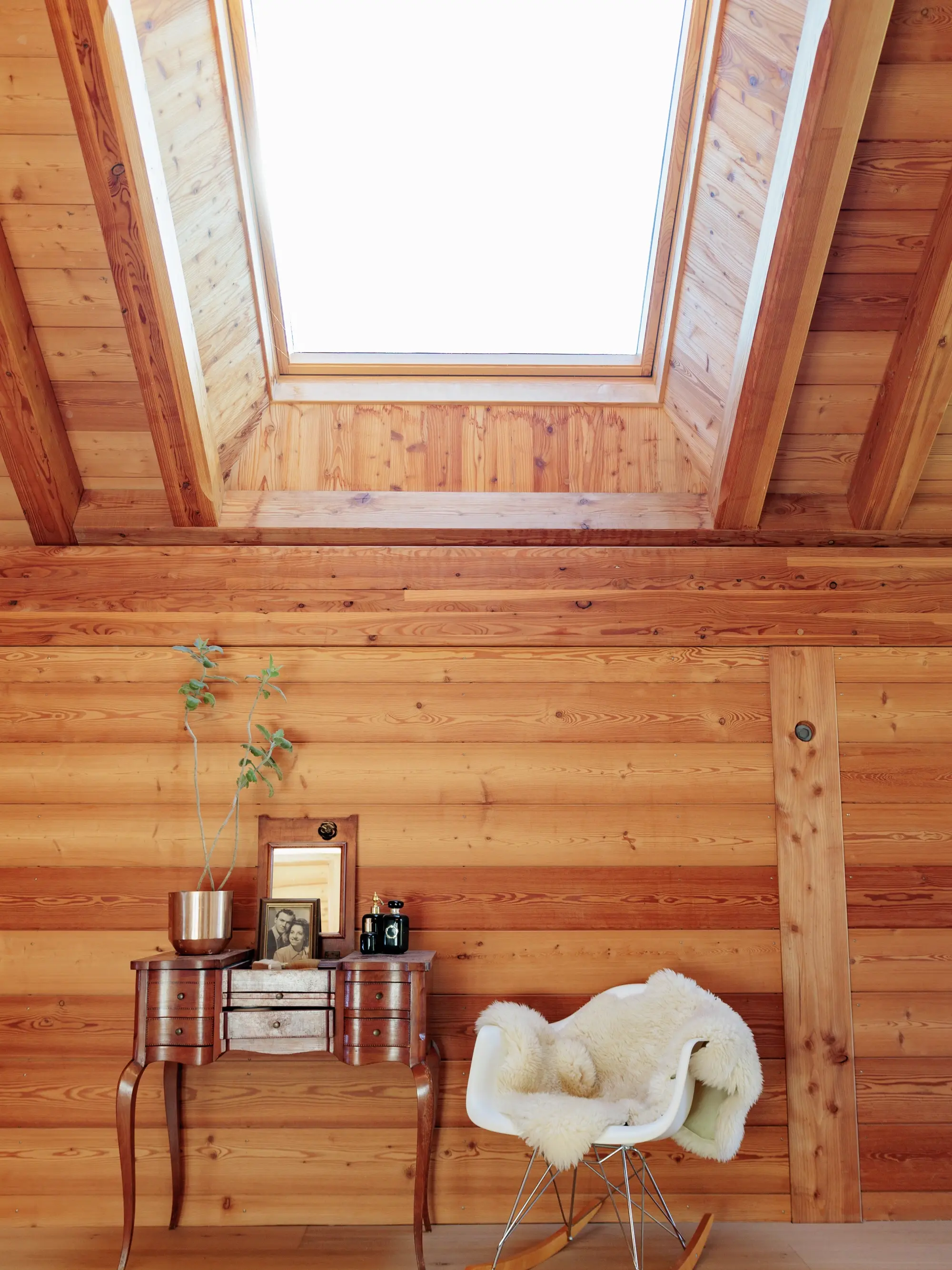 Coin de comble avec bureau en bois, chaise moderne avec peau de mouton, sous une fenêtre de toit VELUX.