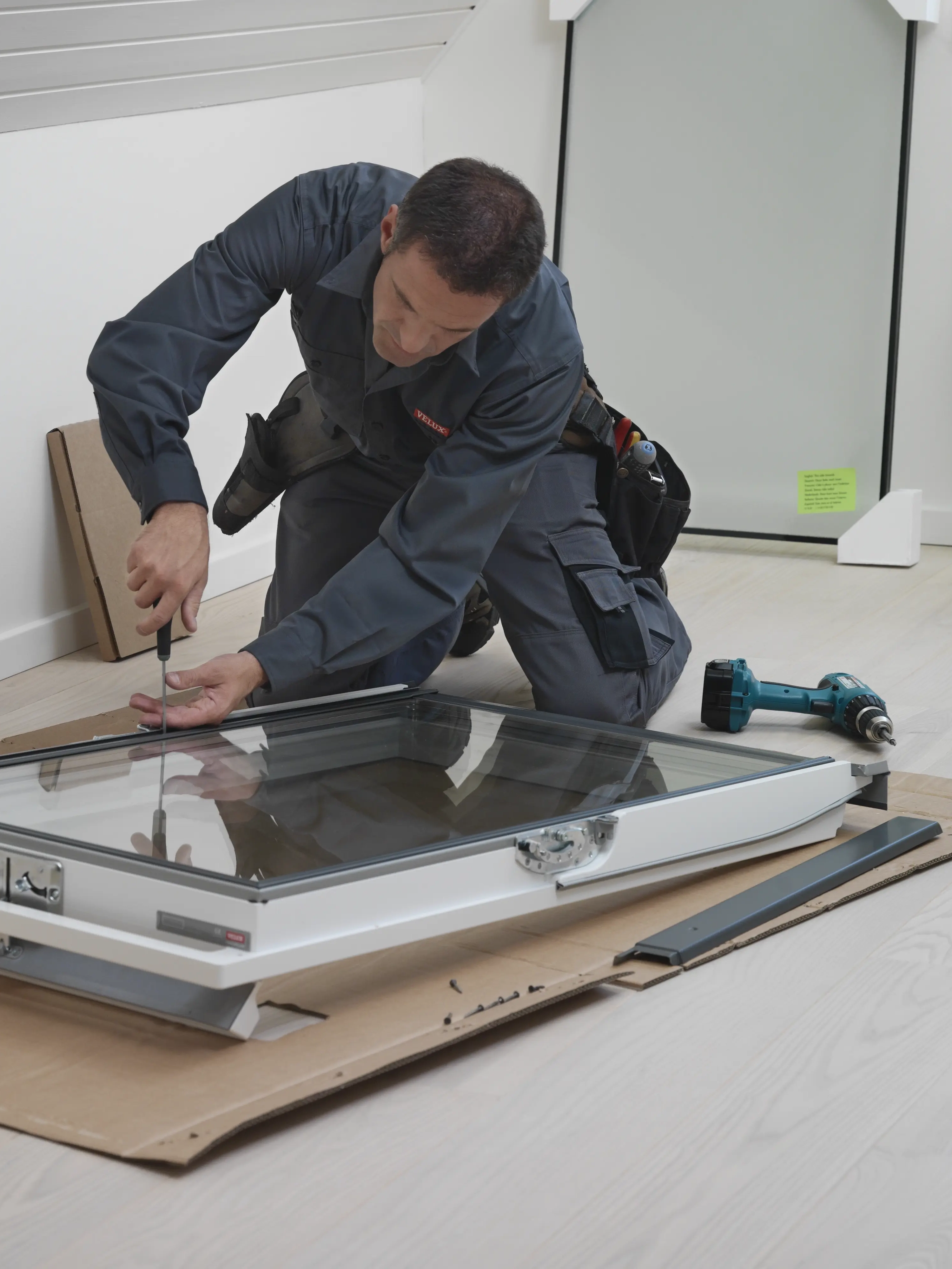 Installer assembling VELUX roof window in attic room with sloped ceiling.