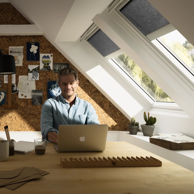 Attic workspace with sloped ceiling and VELUX roof windows, natural light entering.