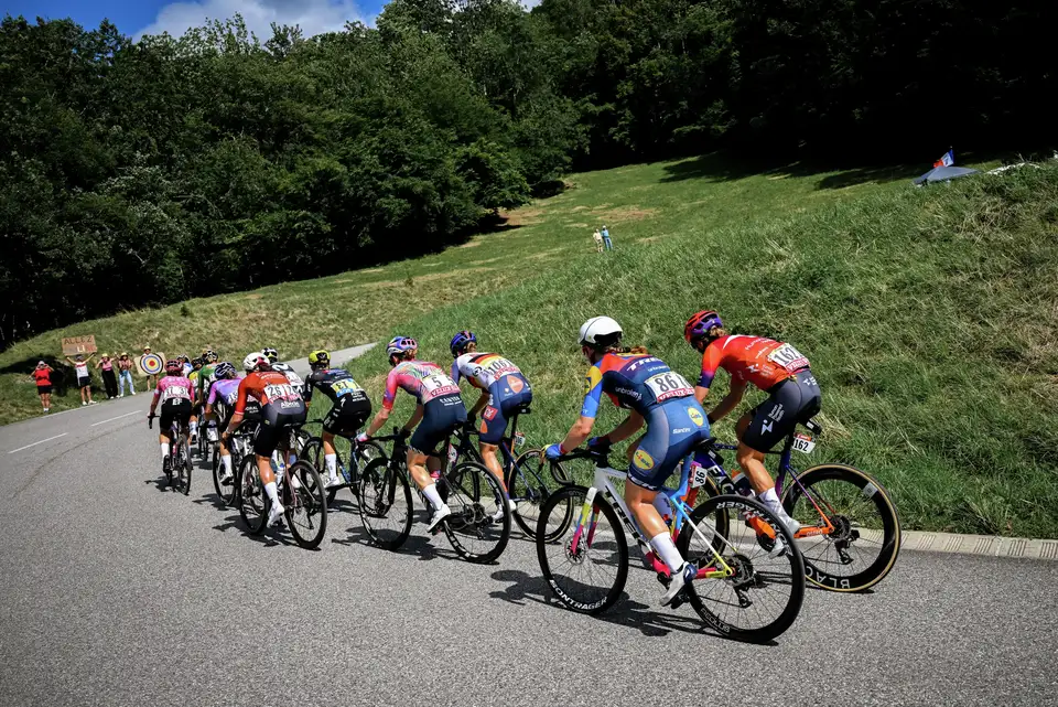 Kolesarke drvijo navzdol po vijugasti cesti, gledalci jih navdušeno spodbujajo med dirko Tour de France Femmes avec Zwift.