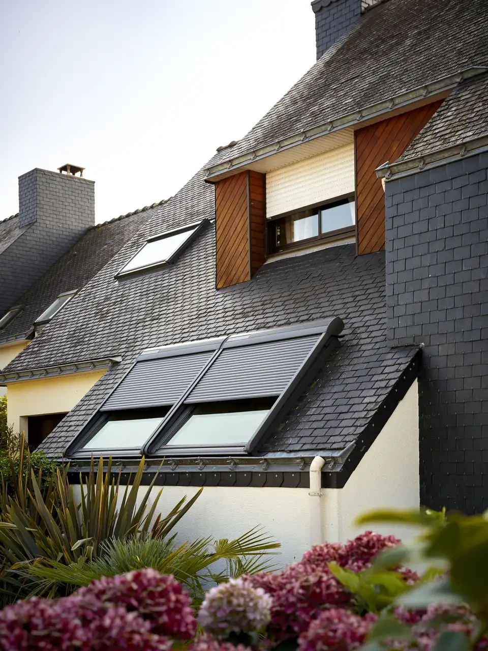 Deze afbeelding toont een modern architecturaal ontwerp van een huis met een combinatie van een traditioneel dak en hedendaagse elementen, wat een interessant samenspel van oude en nieuwe stijlen illustreert. Het VELUX dakvenster voegt een moderne toets toe aan de traditionele structuur.