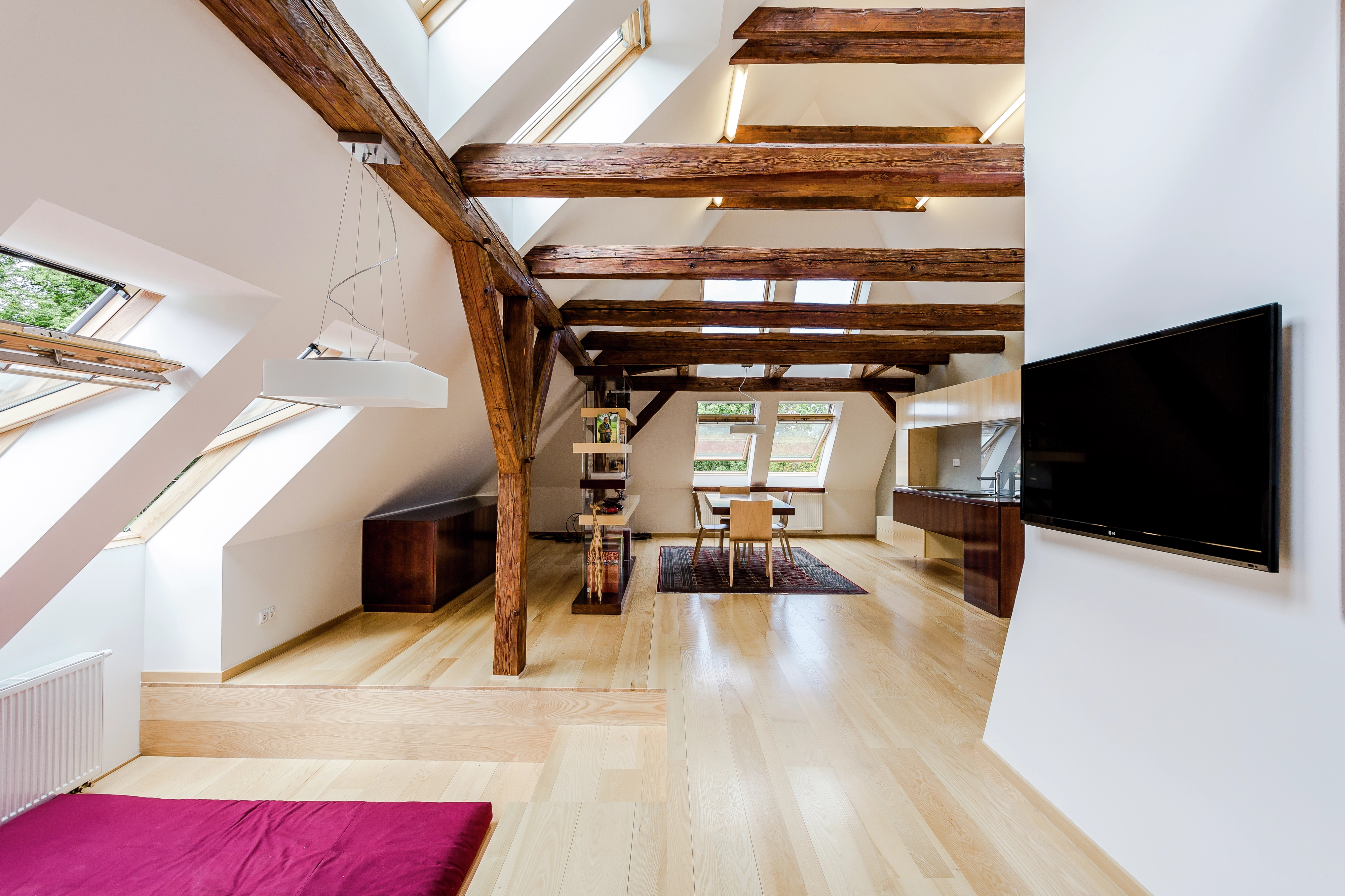 Open space con travi a vista, pavimento in legno e finestre per tetti VELUX sovrapposte per illuminare e ventilare l’ambiente