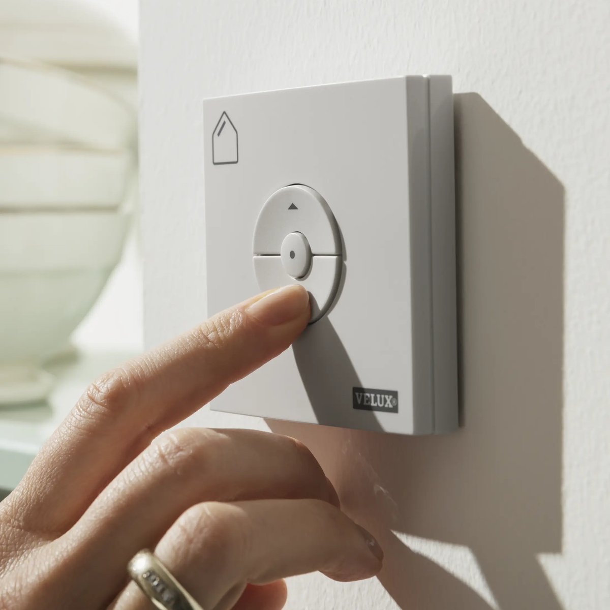 Hand adjusting VELUX control panel in a modern kitchen setting.